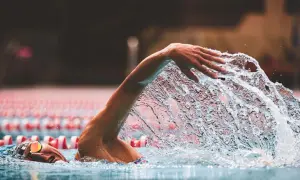 A swimmer's arm slices through the water, creating a dramatic splash during a powerful stroke. The focus is on the dynamic movement as they swim.