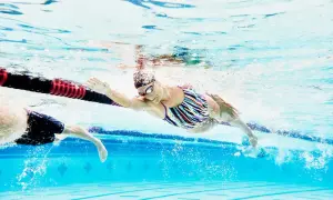 A swimmer in a colorful suit glides through the water, her arm extended, during a recovery swim workout.