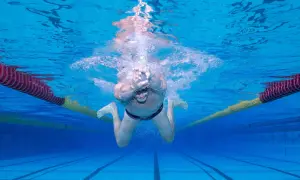 Underwater view of a man performing the breast stroke in a swimming pool, with lane lines and buoys visible.