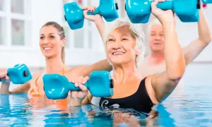 Seniors and a younger woman enjoy pool exercises, lifting blue dumbbells for a refreshing workout.