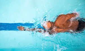 A swimmer powers through the water, creating splashes. This image inspires questions about how long to swim for exercise.