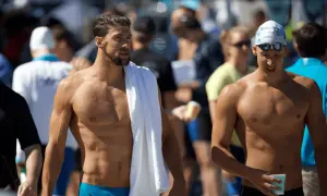 Two muscular men, one with a towel draped over his shoulder, showcase the lean physique of a swimmer body vs. a gym body.