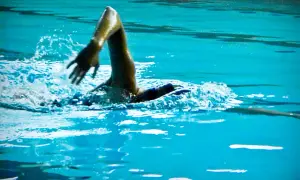 Swimmer's arm in a powerful high elbow catch, slicing through the turquoise water with a splash.