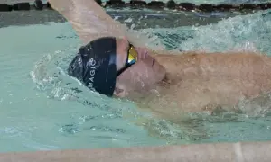 Swimmer executing a backstroke flip turn, water splashing around their head and goggles.
