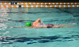 A swimmer in a green cap performs a front crawl swim, their body streamlined as they glide through the turquoise water.