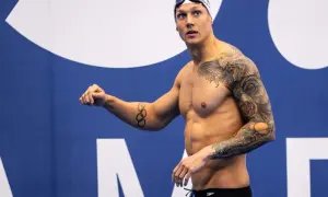 A muscular swimmer with extensive tattoos, including Olympic rings, prepares for a race, showcasing his dedication to swim conditioning.