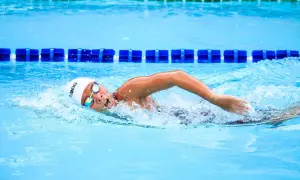 Swimmer in a white cap and goggles executes a powerful american crawl stroke, churning the bright blue water.