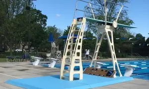 A tall, cream-colored high diving board stands ready for action next to a bright blue pool.