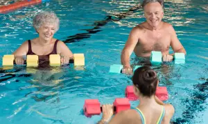 Smiling seniors and a younger woman enjoy water aerobics with buoyant dumbbells. A perfect before and after workout for all ages.