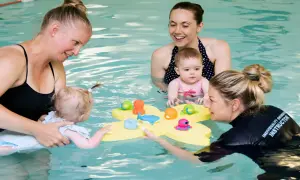 Moms and instructors in a pool with toddlers, playing with bath toys. The question of how many swim lessons does a toddler need is a common one for parents.