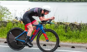 Athlete in a road triathlon, focused and aerodynamic on a blue and red Specialized bike, with a lake in the background.