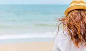 Woman with red hair in a straw hat on the beach, wondering how soon can I swim after coloring my hair.