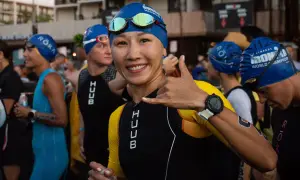 A smiling woman in a blue swim cap and yellow and black triathlon suit gives a shaka sign, ready for the honu triathlon.