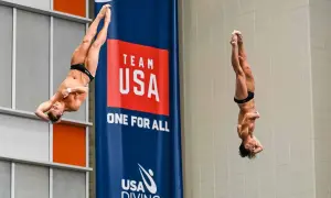 Two divers perform a synchronized high dive, suspended mid-air in a dramatic pose against a "Team USA" banner.