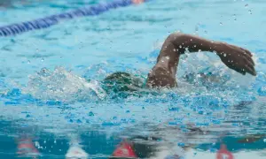 A swimmer powers through the water, mid-stroke, during an intense 1 hour swim workout. Splashes and bubbles fly.