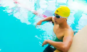 A young swimmer in a yellow cap and goggles rests by the pool edge, contemplating how much do swim instructors make.