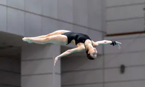 A diver executes a perfect pike position mid-air, body bent at the hips with legs straight and together.