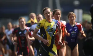 Katie Zaferes, number 01, leads a pack of triathletes in a race, her yellow and black suit featuring a rhino logo.