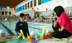 A swim instructor in a pink shirt and hijab coaches young children in a pool, demonstrating the rewarding nature of swim instructor jobs.