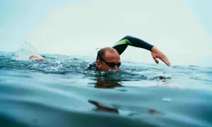 Swimmer in goggles and wetsuit performs swim drills, with one arm extended and splashing water.