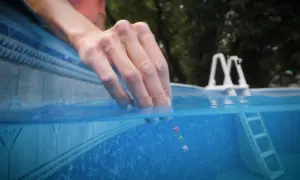 A hand dips a test strip into a pool, checking if chlorine kills fungus and other contaminants.