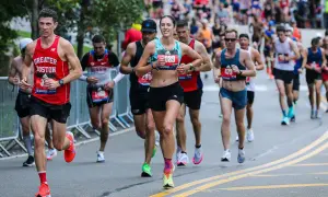 Runners in a marathon, some wearing "Greater Boston" gear, push through the race. The image captures the intensity of the iron man marathon length.