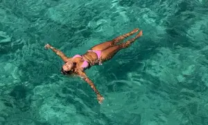 A woman in a pink bikini floats on her back in clear turquoise water. She's enjoying the water, and yes, you can swim with a tampon.