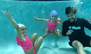 A swim instructor smiles while teaching two young girls how to teach toddler to hold breath underwater.