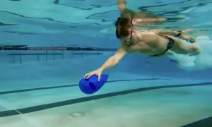 Man swimming underwater with a blue kickboard, practicing his kickboard swim technique.