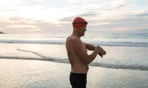Man in swim cap checks watch on beach, ready for his swim. Early morning or late evening might be the best time to swim for weight loss.