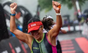 A triumphant athlete celebrates crossing the finish line of an Ironman length race in the rain.