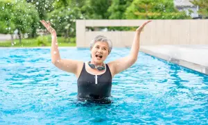 Joyful senior woman splashing water in a pool, enjoying her beginner swim workout.