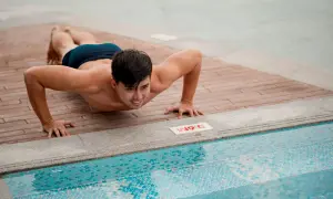 Man doing push-ups on a wooden deck next to a swimming pool.