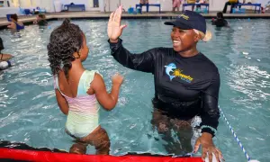 A swim instructor gives a young girl a high-five during swim stroke lessons.