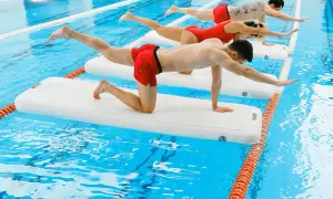 Three people practice aqua gym on inflatable mats in a pool, balancing in a plank-like pose.