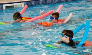 Children in goggles and swim aids enjoy a swim lesson, practicing their strokes in a bright blue pool.