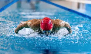A swimmer in a red cap and goggles powers through the water, showcasing the strength and full-body engagement of breaststroke benefits.