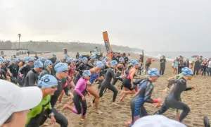 Athletes in wetsuits and blue caps sprint on the sand at the Zuma Beach Triathlon, starting their race with determination.