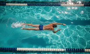 A swimmer glides through a pool, executing a perfect stroke as part of their swim workout plan. Sunlight dances on the water's surface.