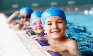 Happy kids in blue swim caps at swim lessons for kids, smiling by the pool edge.