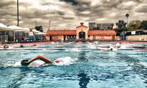 Swimmers race in an outdoor pool under a dramatic cloudy sky, enjoying a refreshing morning swim.