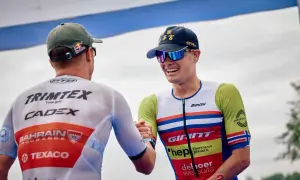 Gustav Iden, a triumphant triathlete, shares a handshake after a race, his smile wide and his racing suit vibrant.