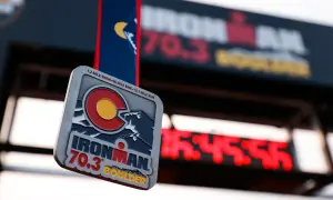 Ironman 70.3 Boulder medal hangs in front of a finish line clock. The medal features the Colorado flag and mountains.