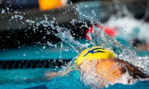 A swimmer in a yellow cap with a blue lightning bolt, mid-stroke, creating a dramatic splash. This captures the intense swolf meaning of speed and power.