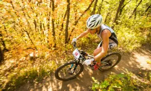 Athlete races through an autumn forest during an off road triathlon, navigating a dirt path with colorful foliage.