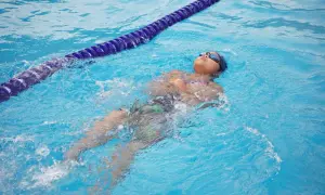 A child practices how to tread water in a pool, floating on their back with goggles on.