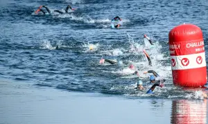 Athletes compete in a triathlon, their triathlon swim strokes creating splashes as they navigate the water around a red buoy.