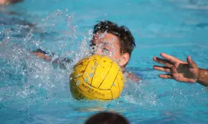 A young player in a water polo match splashes water as they go for the ball.
