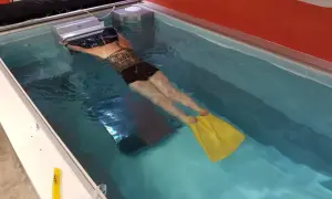 Woman with yellow fins practicing her leg kicking in a swim spa.