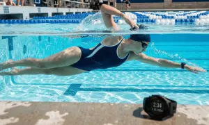An adult woman is learning to swim, powering through the water in a competitive pool. A smartwatch on her wrist tracks her progress.